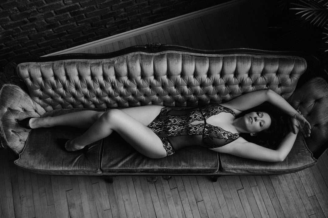 full body boudoir shot of woman lying on couch in detailed bodysuit lingerie